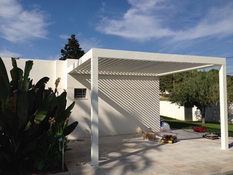 Pérgola bioclimática blanca adosada sobre el porche de un jardín