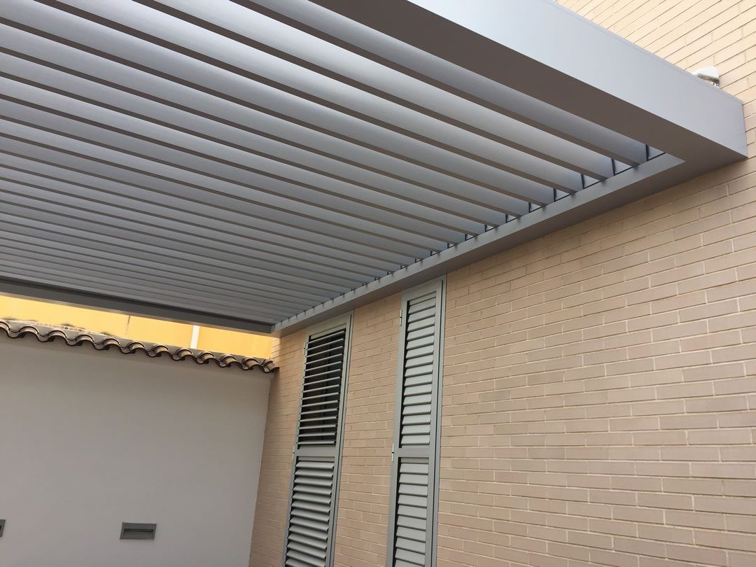 Pérgola de aluminio gris adosada a una fachada de ladrillo