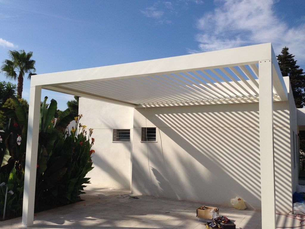 Pérgola bioclimática blanca adosada a la fachada, con las lamas entreabiertas